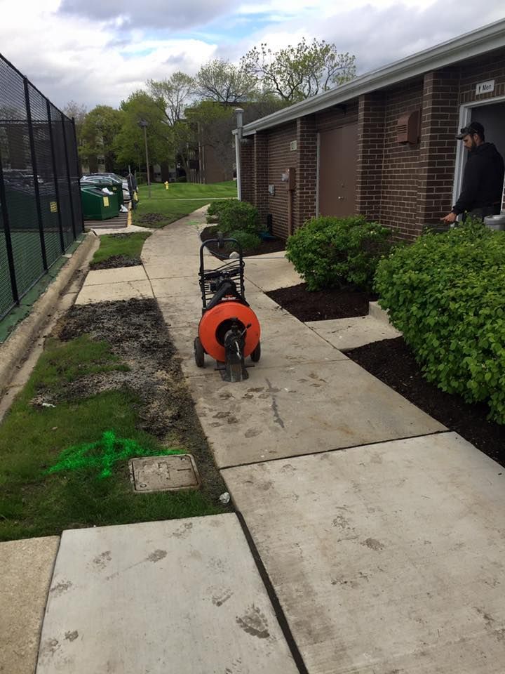 A drain cleaner is sitting on a sidewalk next to a brick building.