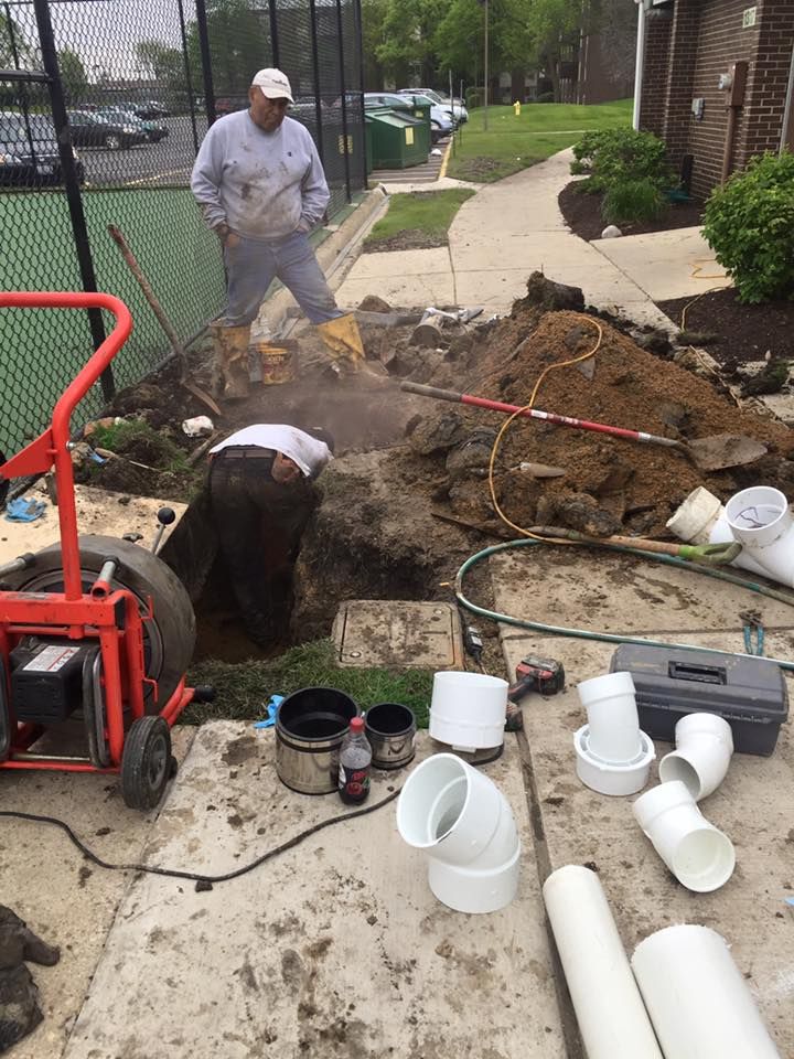 A man is digging a hole in the ground next to a pile of pipes.