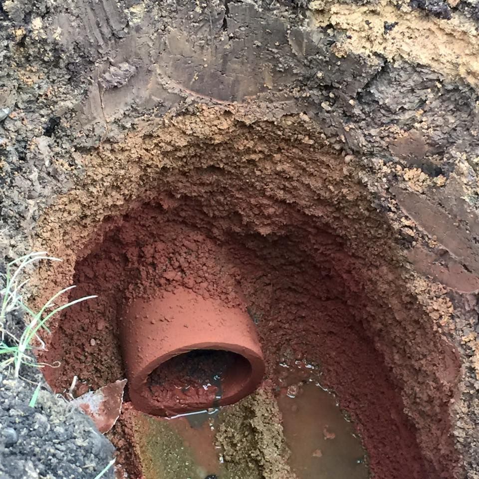 A clay pipe is sitting in the dirt in a hole.