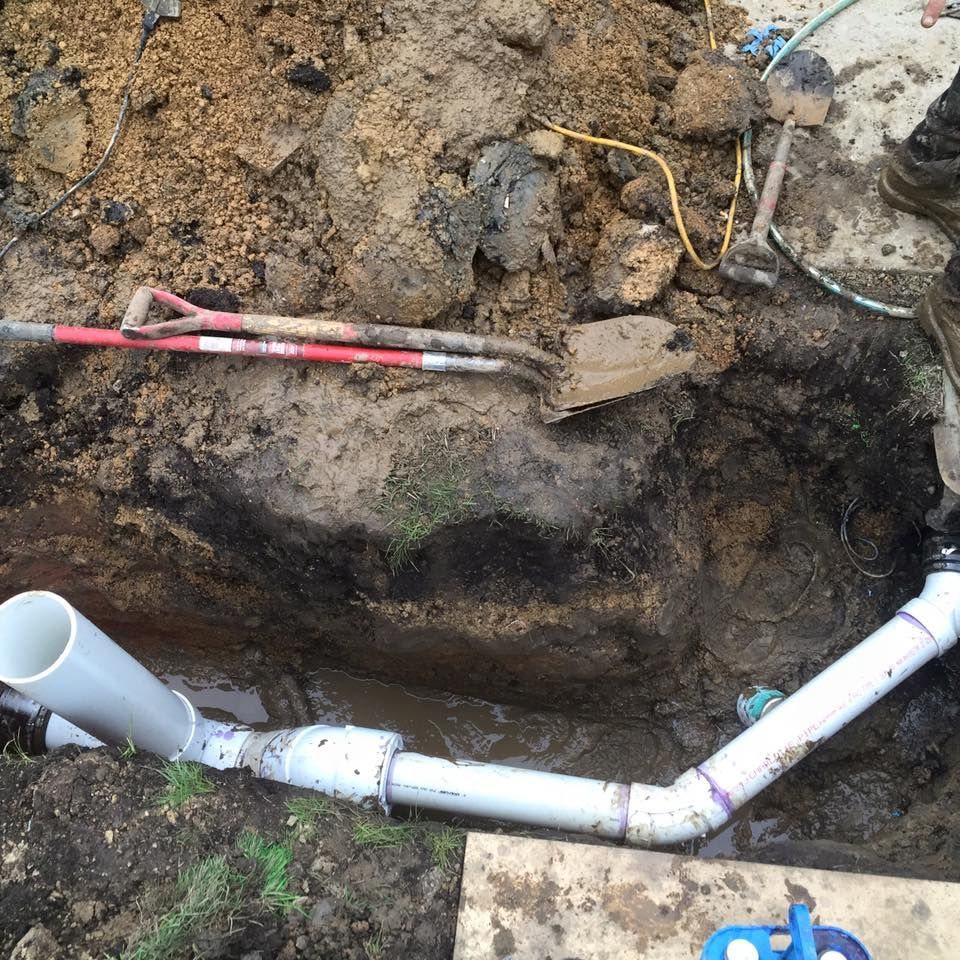 A man is digging in the dirt with a shovel and hose