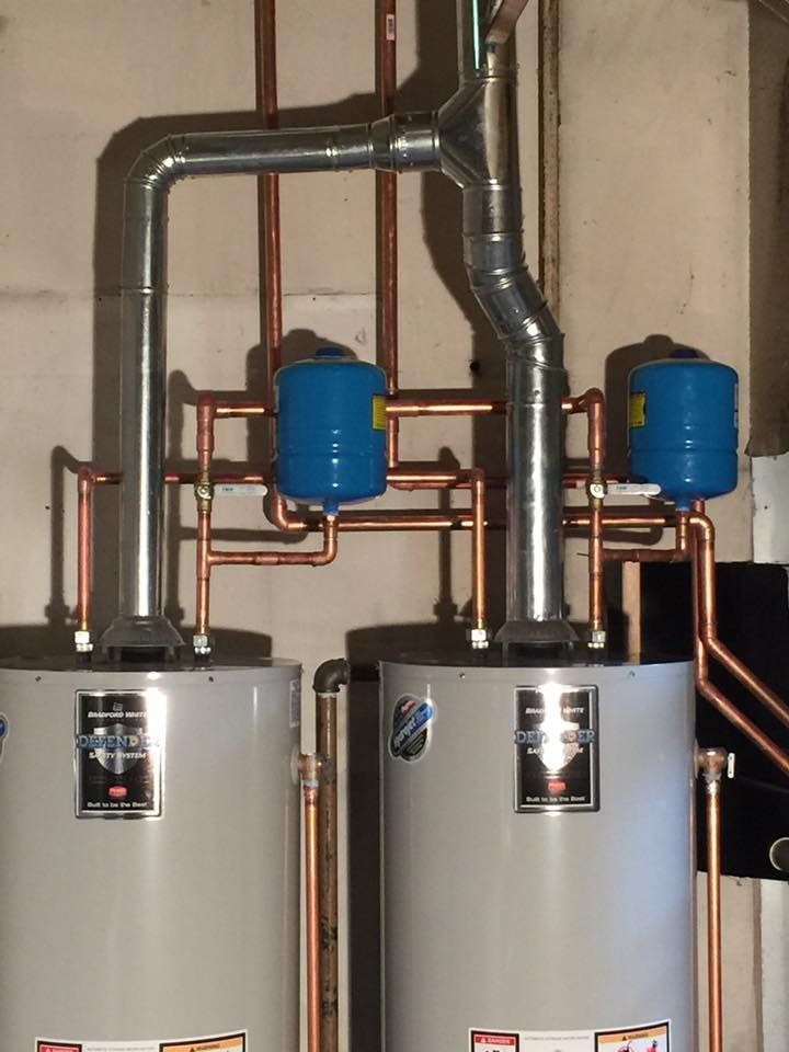Two water heaters are connected to copper pipes in a room