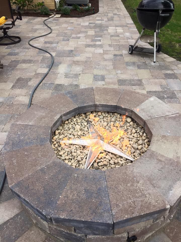A fire pit with a star on it is on a patio next to a grill.