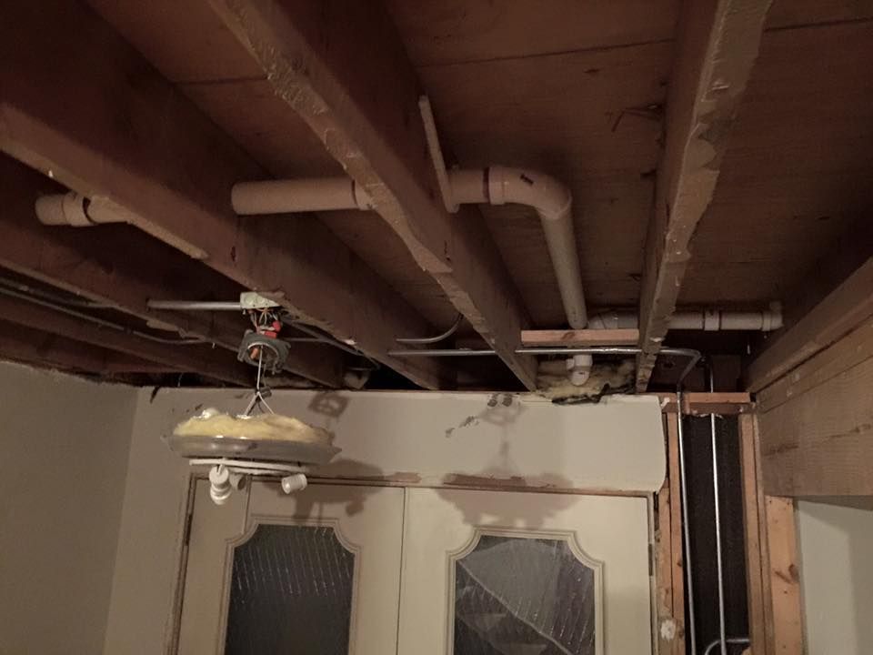 A ceiling with a lot of pipes and wires hanging from it.