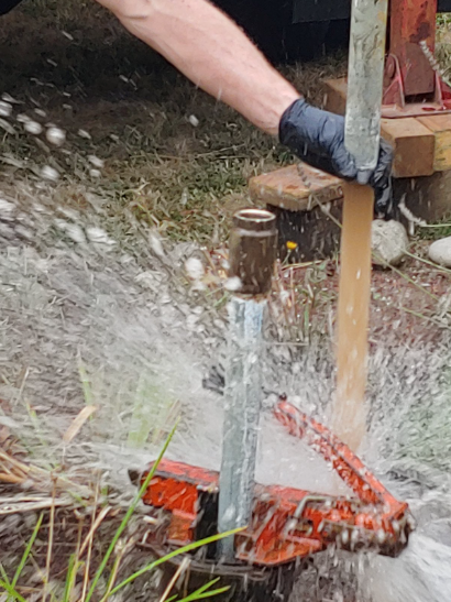 A person in black gloves using a tool to extract water from the ground, water spraying.