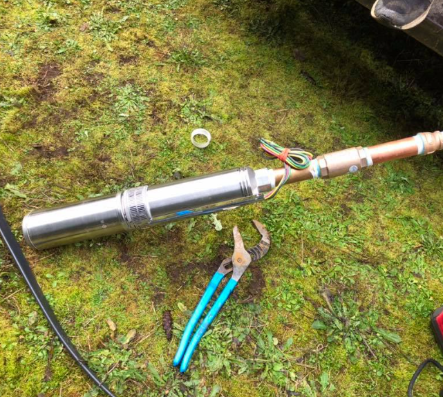 Well pump laid on grass with exposed wires and pliers. Copper pipe attached.