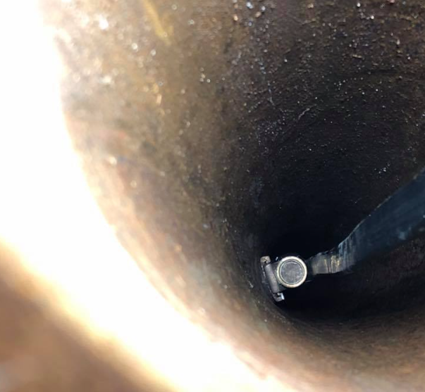 Inside view of a dark pipe with a cylindrical tool inserted at the bottom.