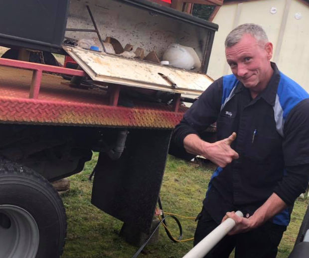 Man giving thumbs up next to a work truck, holding a PVC pipe, smiling.