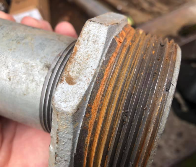 Close-up of a rusty metal threaded pipe fitting, held in a hand.