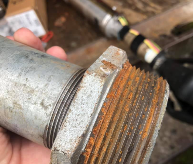 Close-up of a rusty metal pipe fitting with visible threads, held by a hand.