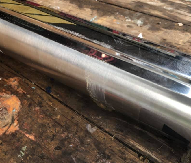 Shiny metal cylinder with a scratched area, lying on weathered wooden boards.