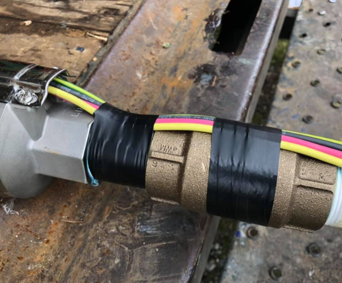 Wires taped to metal pipes and hardware on a metal surface.