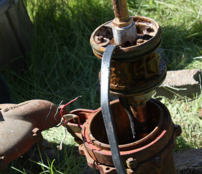 Rusty well pump with exposed interior components and wiring, outdoors.