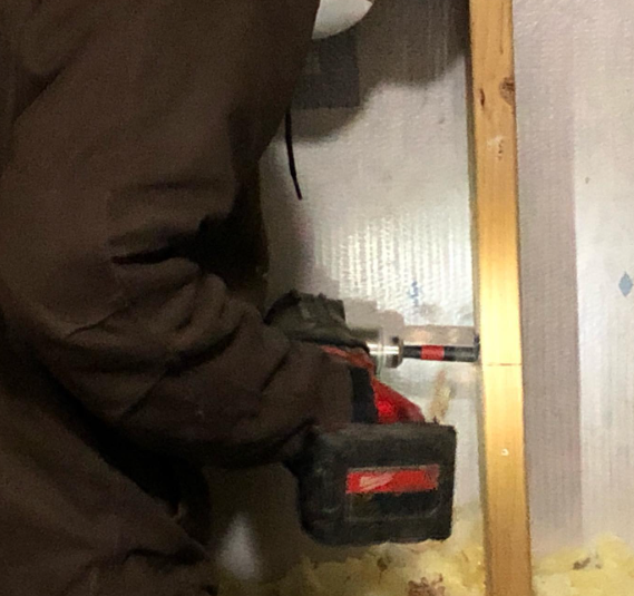 Person using a power drill on a wall. Brown jacket, Milwaukee drill, wood trim.