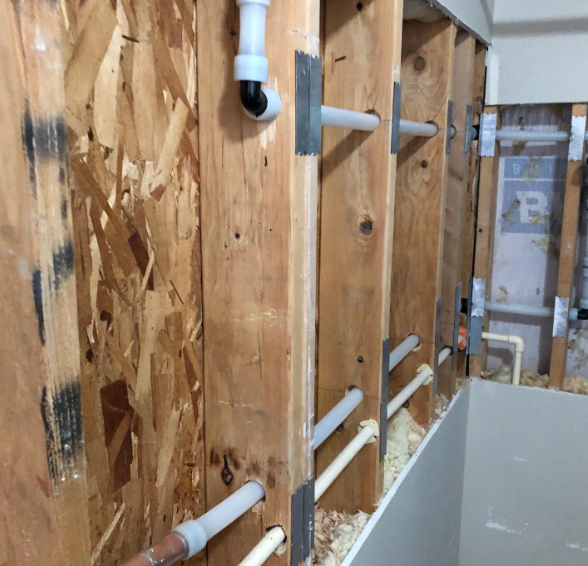 Open bathroom wall showing exposed plumbing and wood framing.
