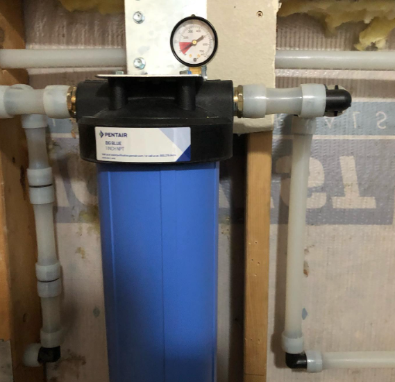 Water filtration system with blue filter, pressure gauge, and white plastic pipes.