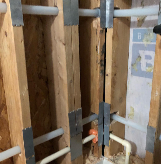 Wooden wall with white pipes secured by metal brackets.