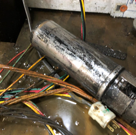 Damaged metal cylinder with wires in a puddle of liquid.