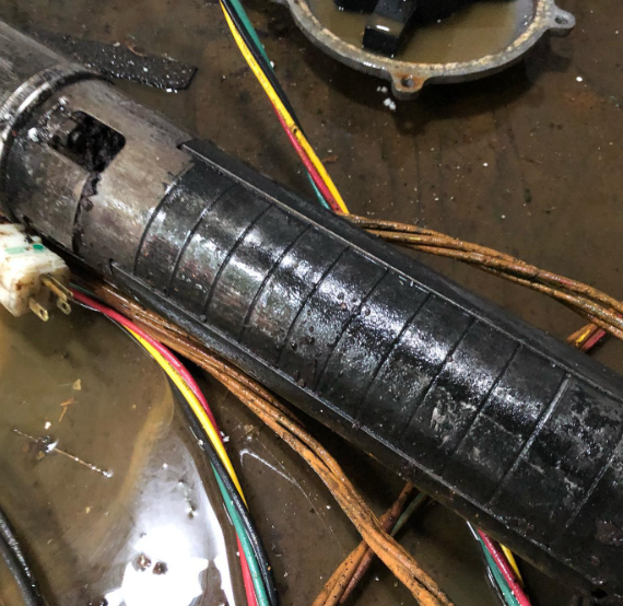 Damaged cylindrical pump component with wires, dark coloring.