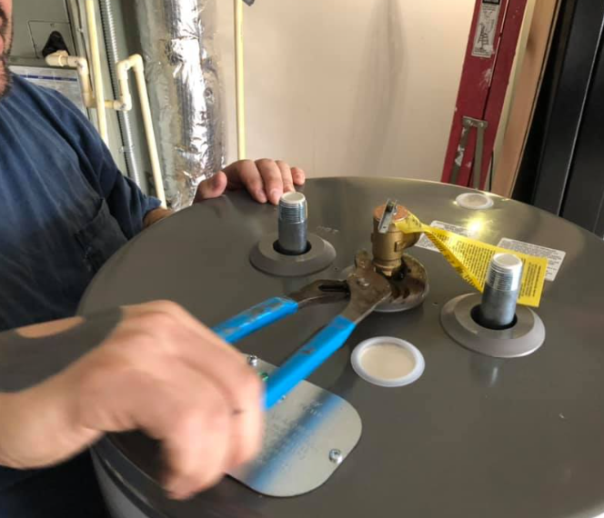 Person using pliers to work on the top of a water heater; silver tank, blue handles.