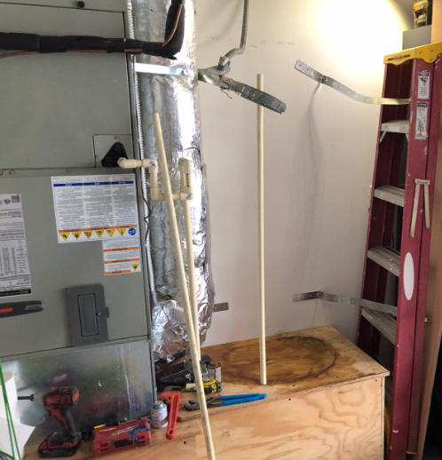 HVAC unit with ductwork, PVC pipes, tools, and a red ladder in an unfinished space.