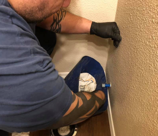 Person wearing black gloves installs something into a wall's corner. Blue cover sits on floor.