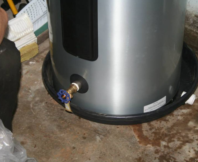 Water heater with a blue valve, sitting in a black basin on a concrete floor.