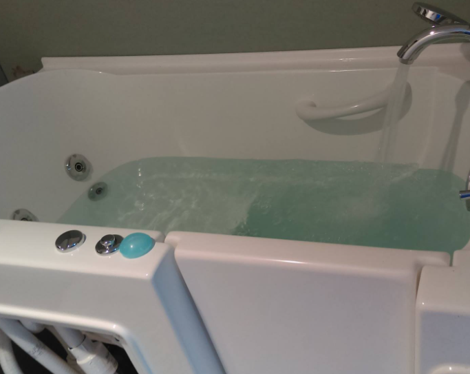 White walk-in bathtub with water, faucet, and control buttons; a handrail is visible.