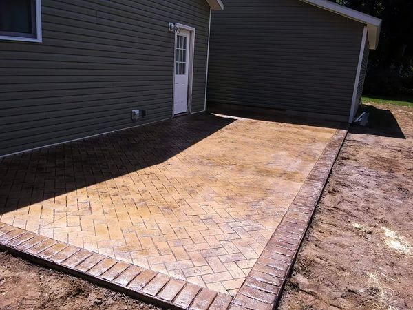 A patio with a herringbone pattern is being built in front of a house.