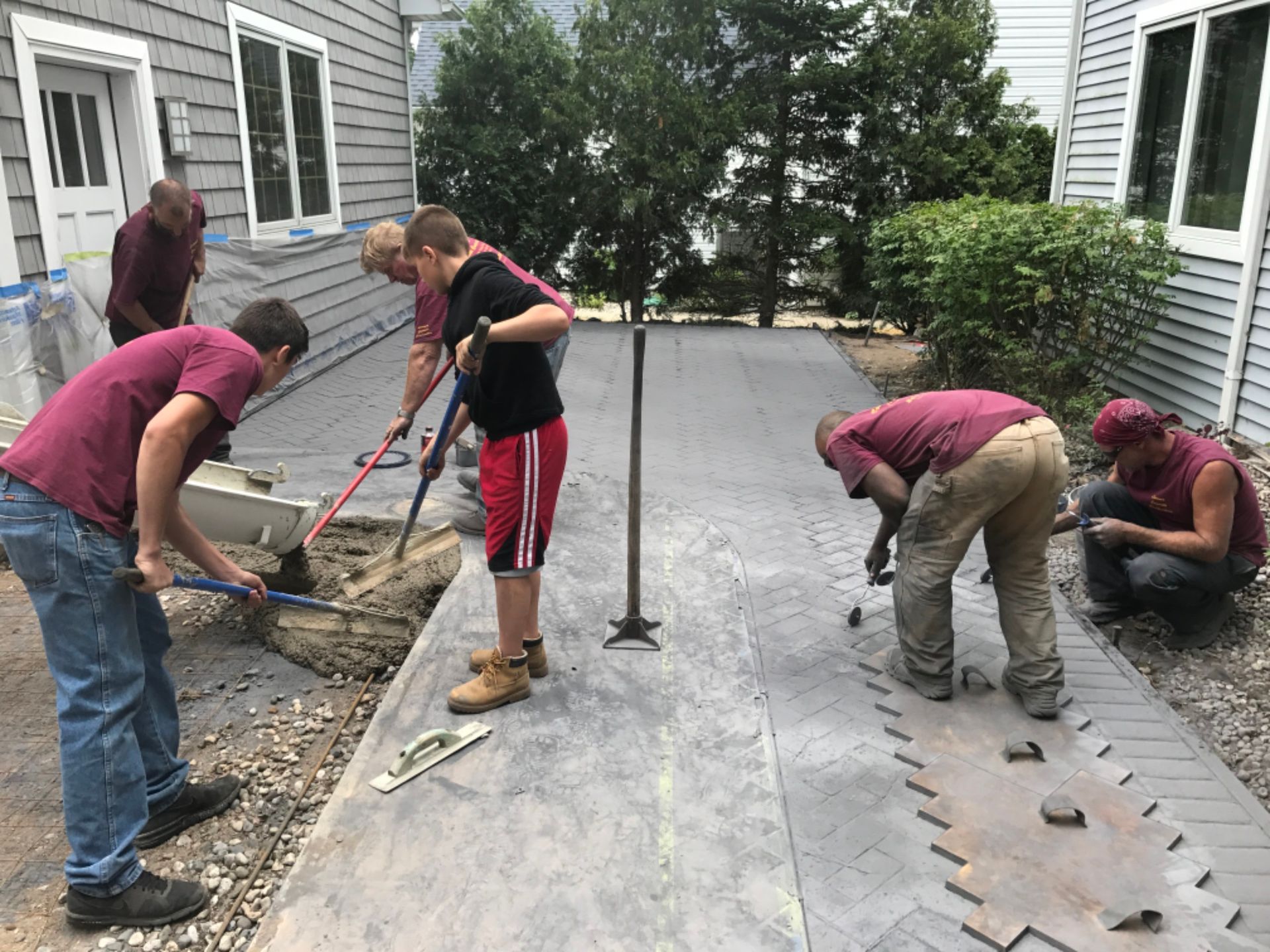 A group of men are working on a sidewalk in front of a house.
