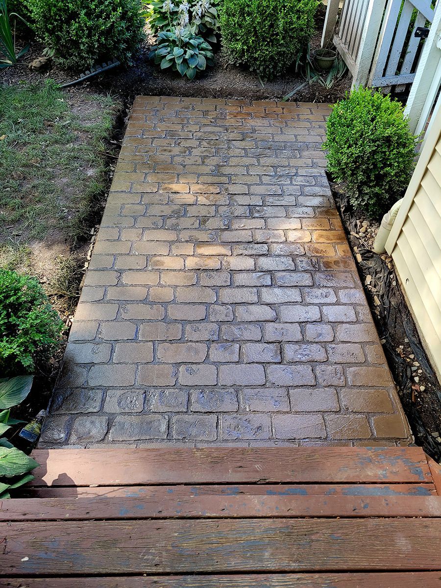 A brick walkway leading to a wooden deck in a backyard.