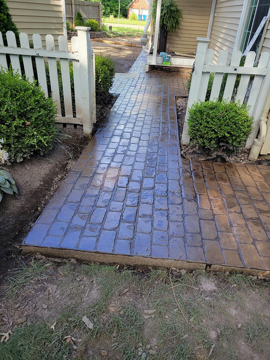 A brick walkway leading to a house with a white picket fence.