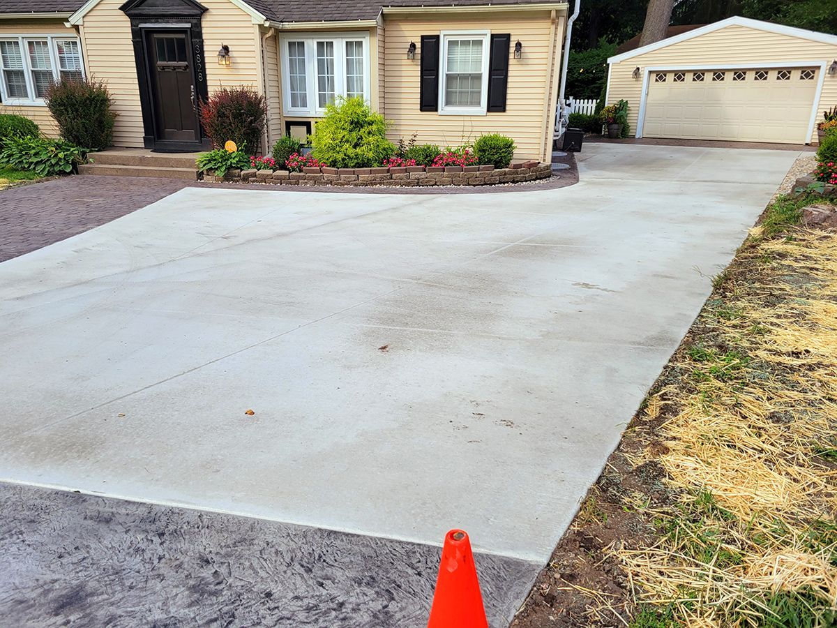 A concrete driveway with an orange cone in front of a house.