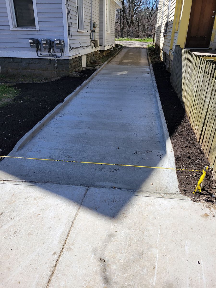A concrete driveway leading to a house with a yellow tape.