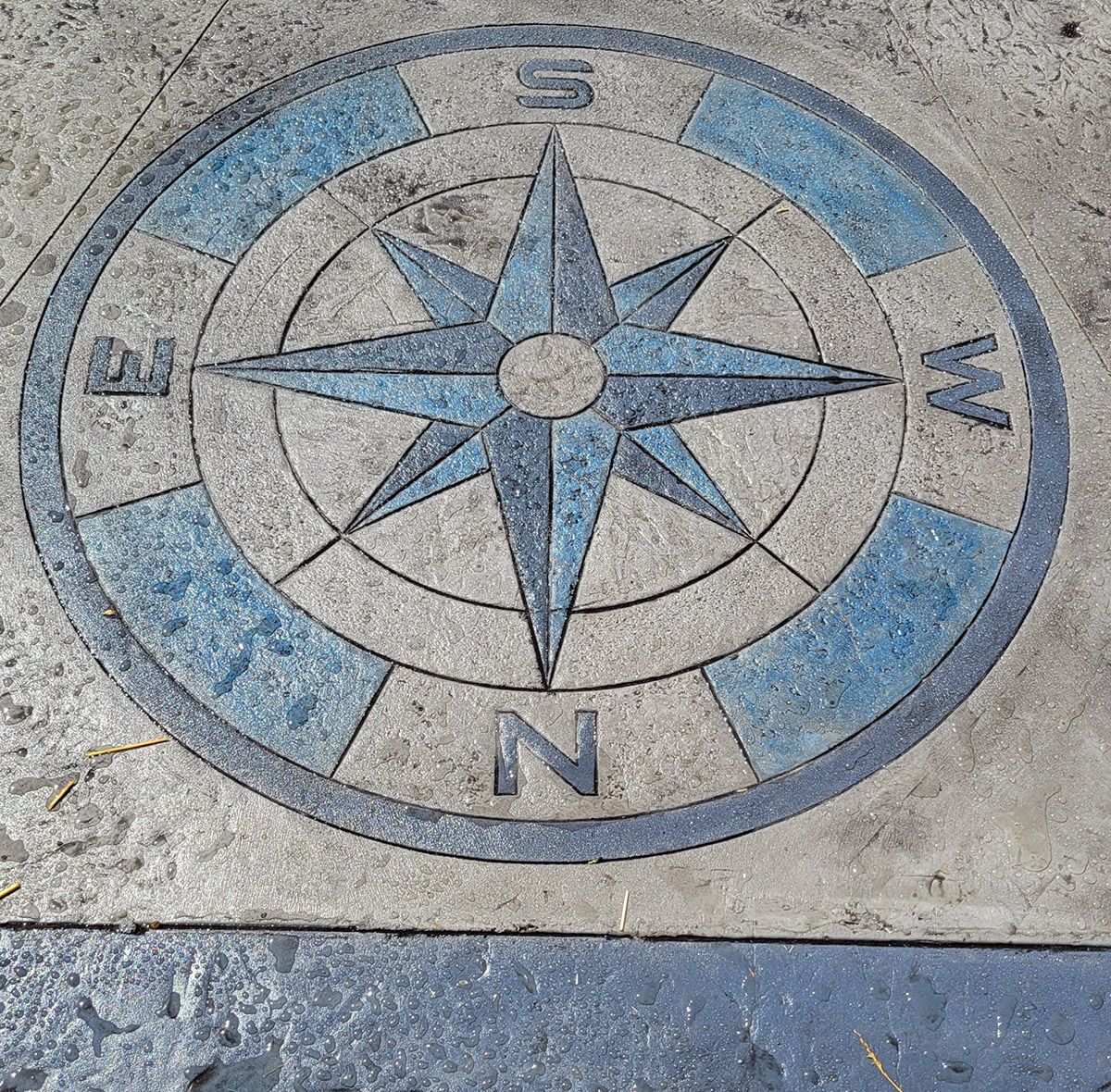 A blue and white compass on a concrete surface