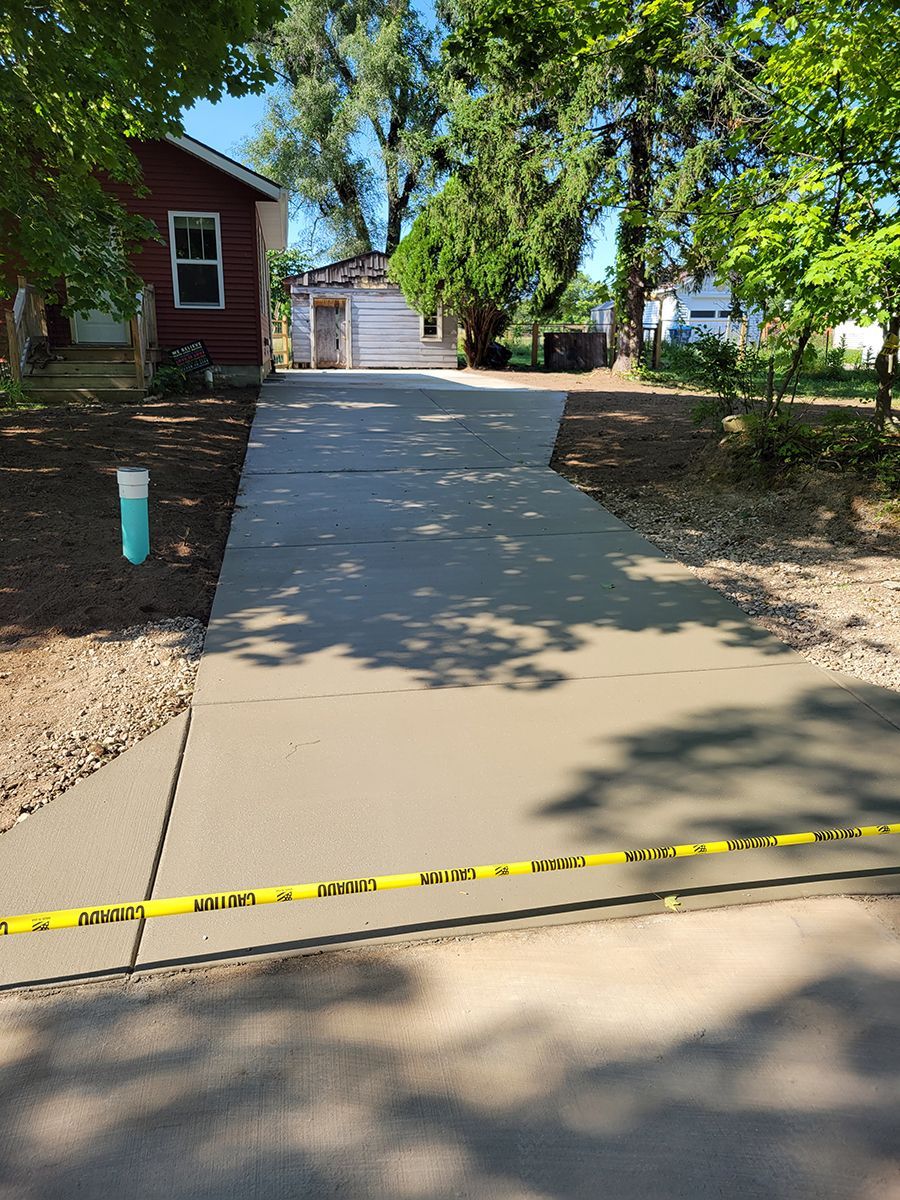 A concrete driveway leading to a house with trees in the background.