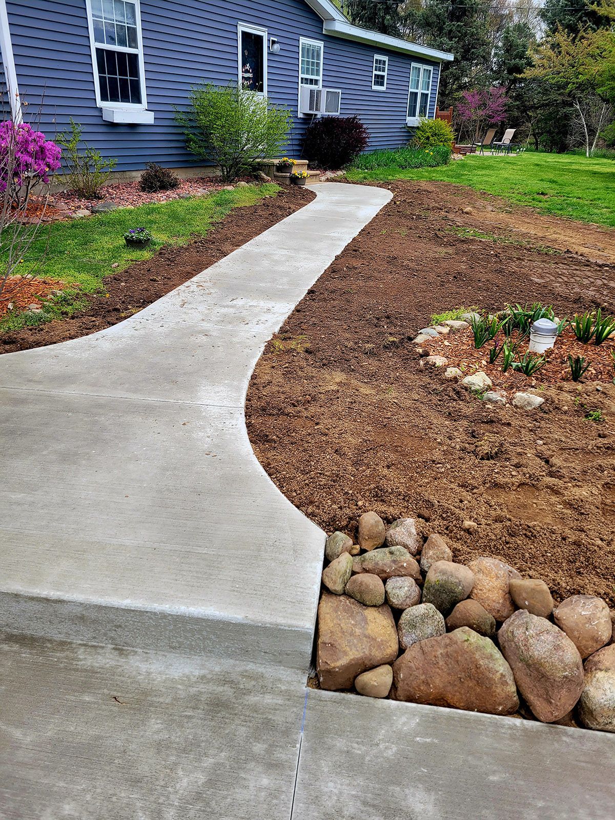 A concrete walkway leading to a house with rocks in the foreground.