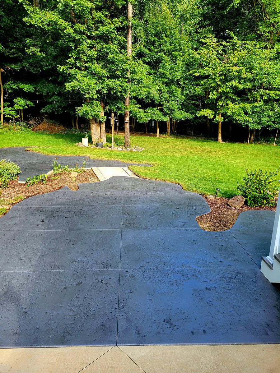 A concrete driveway leading to a lush green yard with trees in the background.