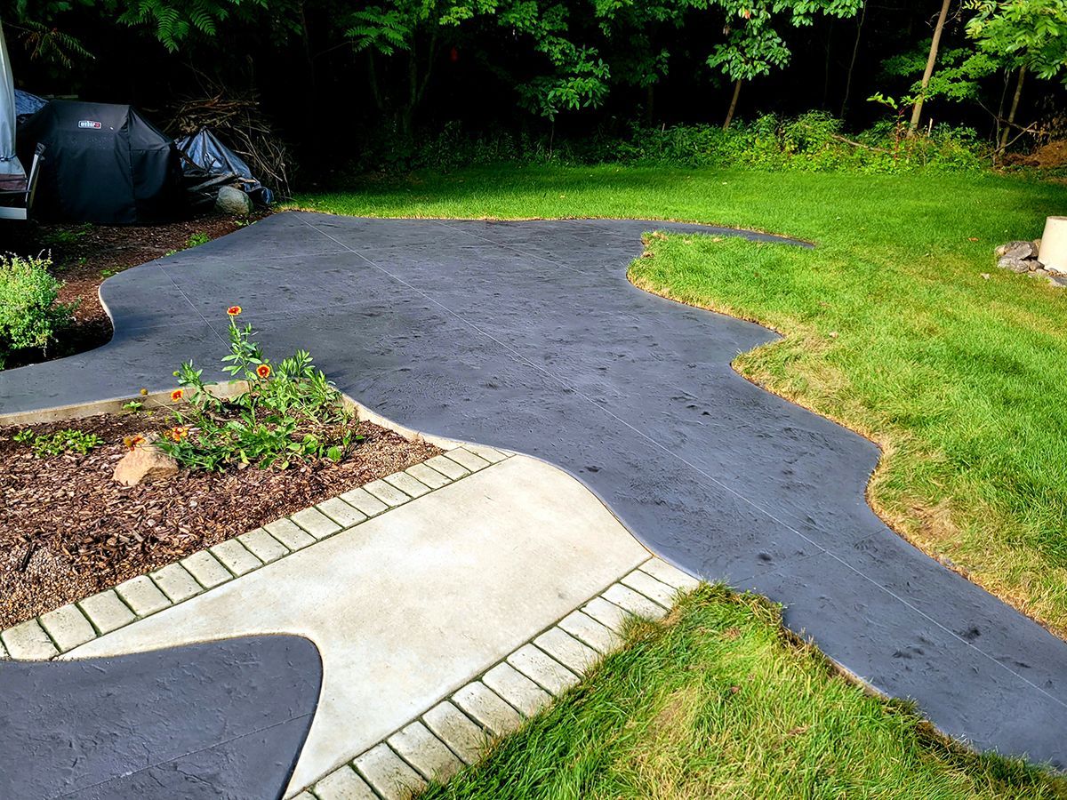 A concrete walkway going through a lush green yard.