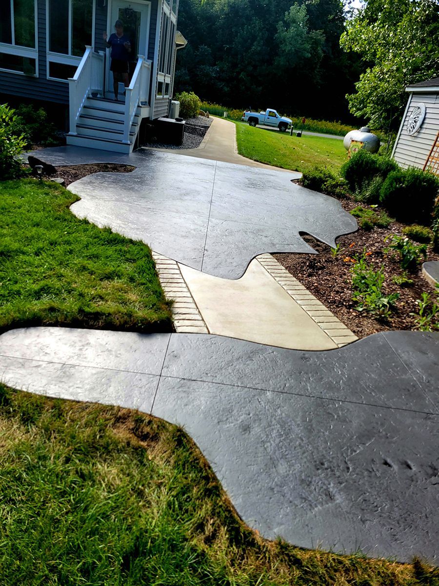A concrete walkway leading to a house in a backyard.