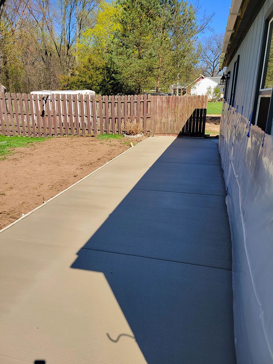 A concrete walkway leading to a house with a wooden fence.