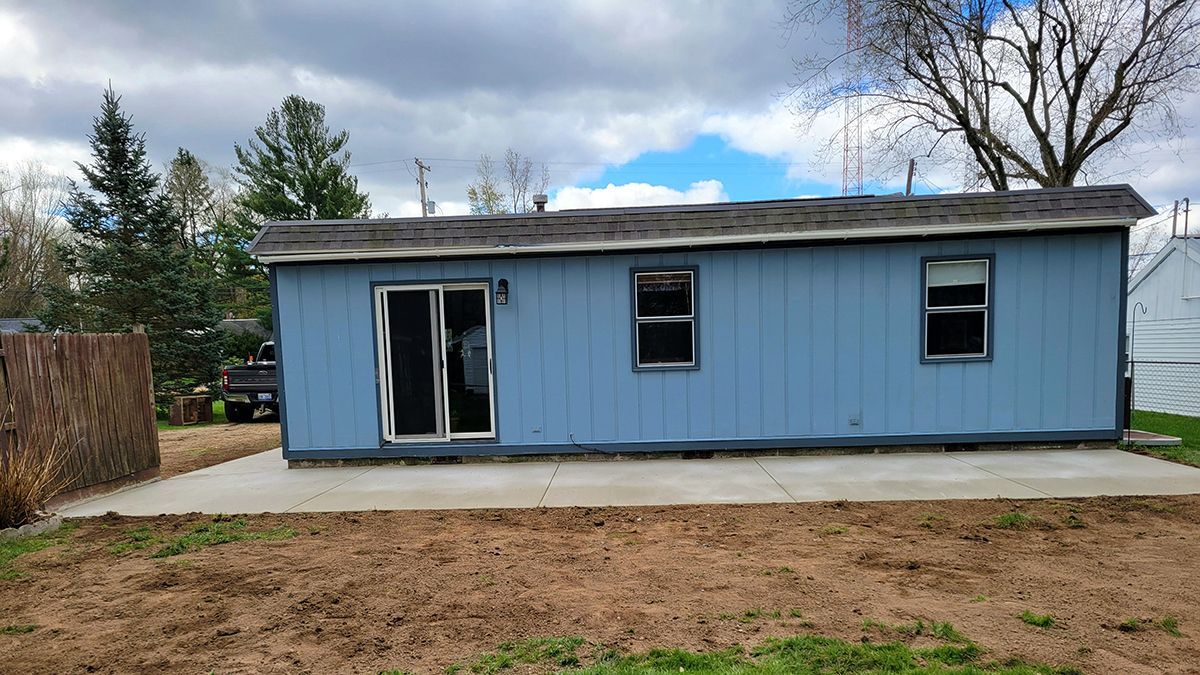 A small blue house is sitting in the middle of a dirt field.
