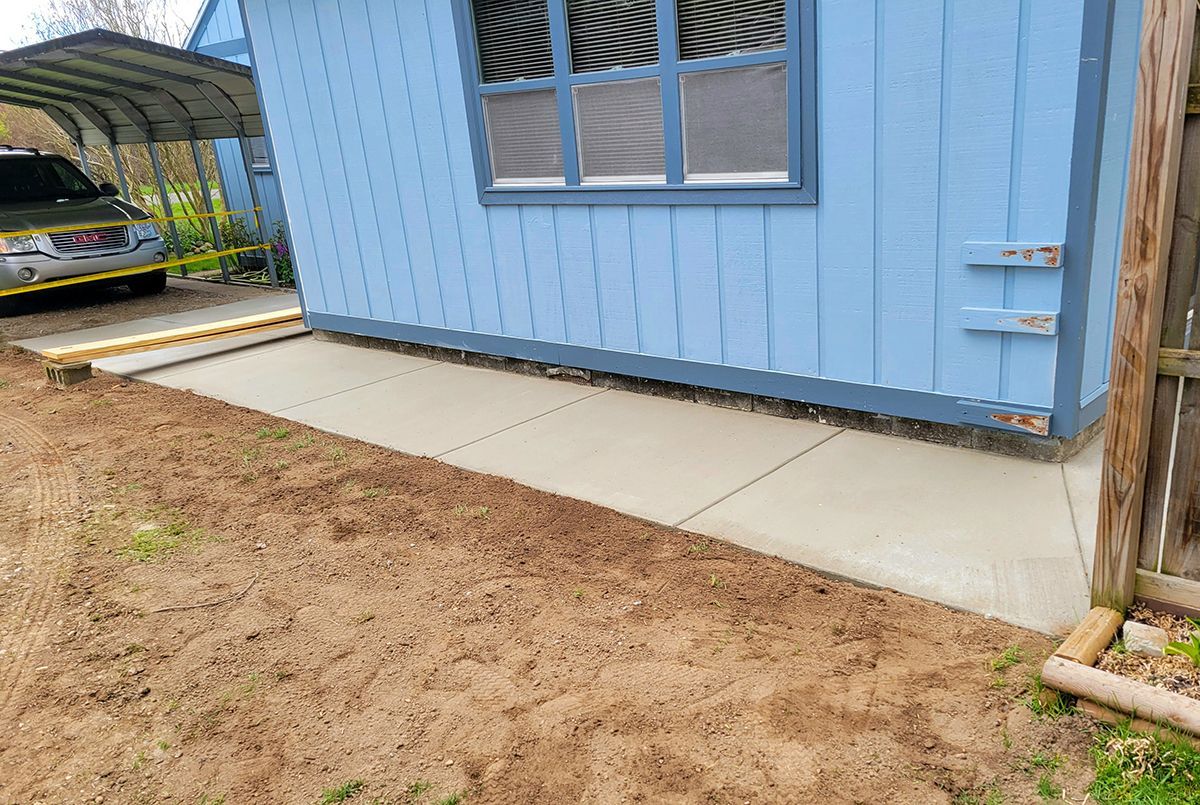 A blue shed with a carport and a concrete walkway in front of it.