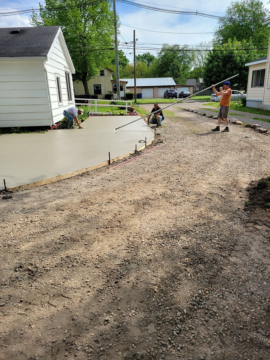 A group of people are working on a concrete driveway in front of a house.
