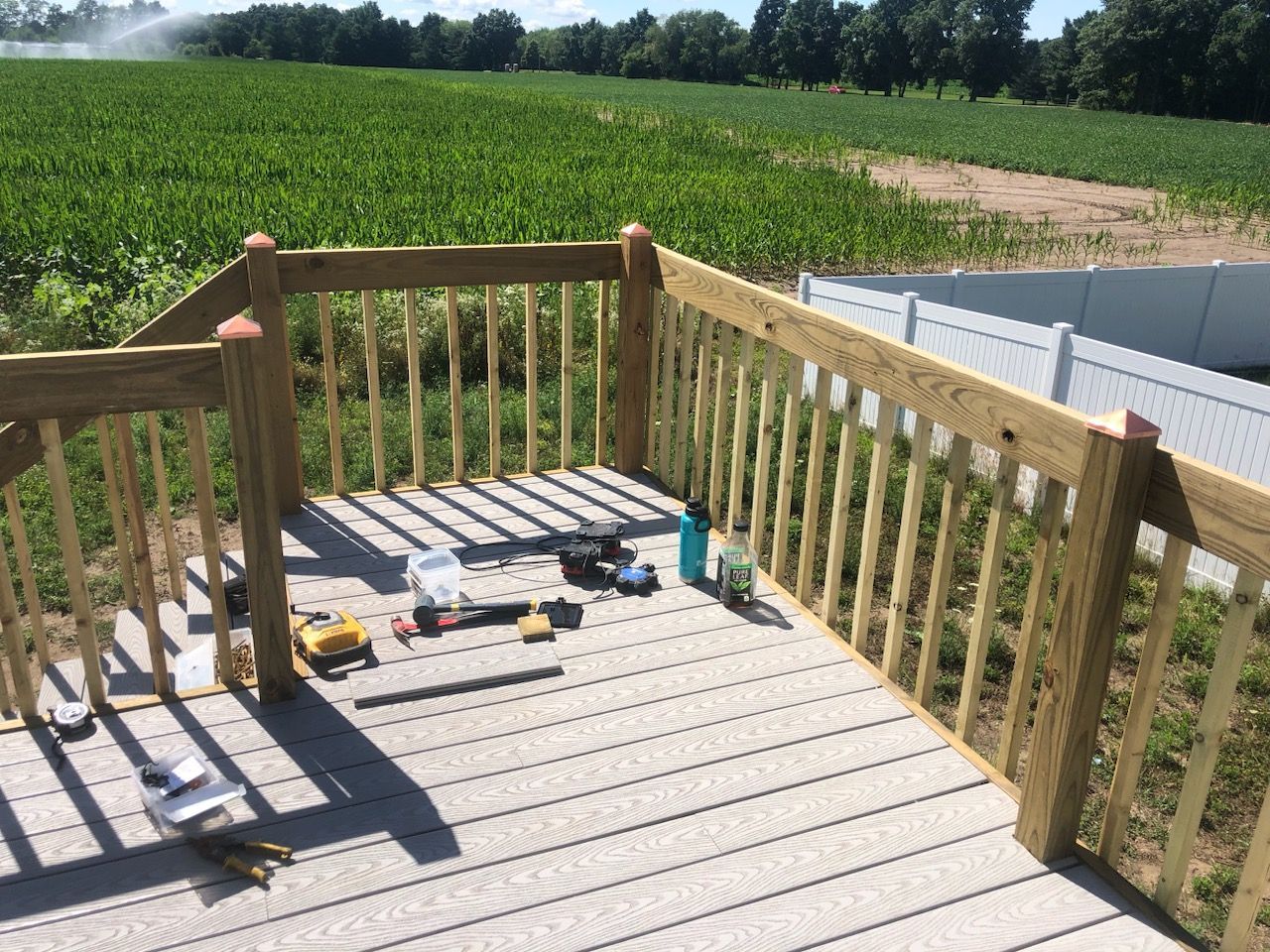 A wooden deck with a fence and a field in the background.