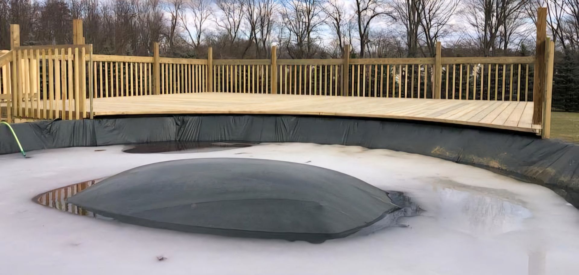 A wooden deck over a swimming pool with trees in the background.