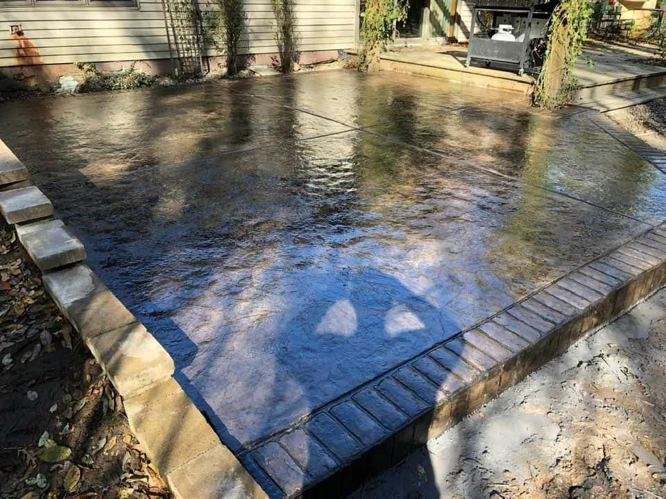 A concrete driveway with a brick border and a reflection of trees in the water.