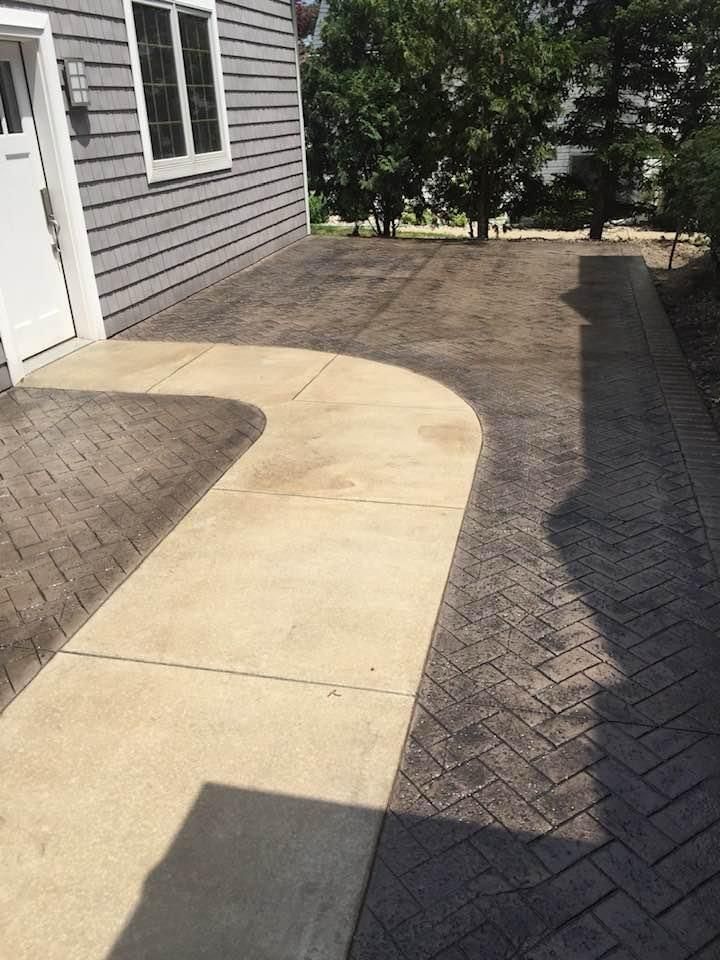 A concrete walkway leading to a house with trees in the background.