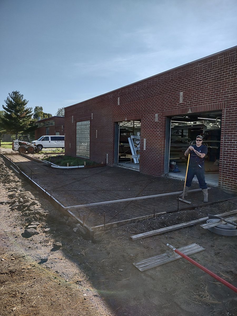 A man is standing in front of a brick building holding a rake.