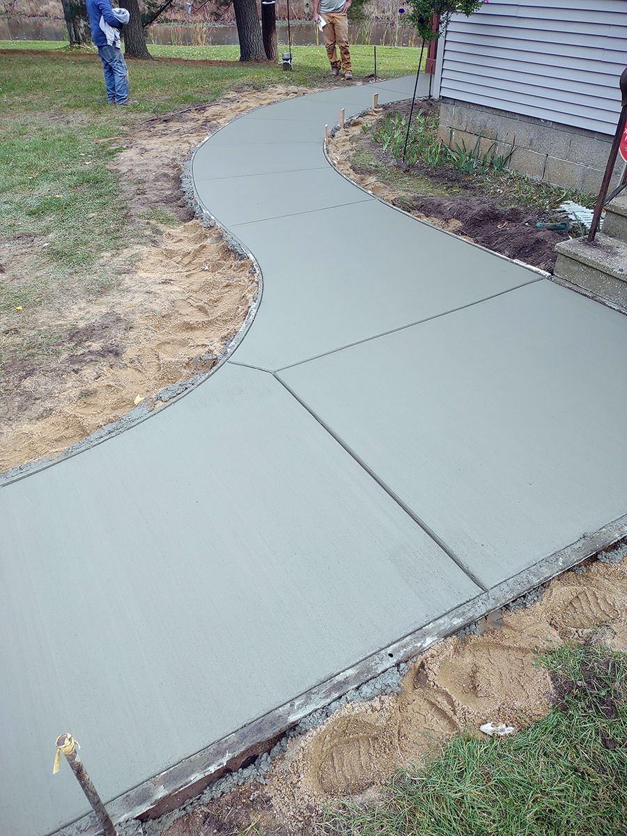 A concrete walkway is being built in the backyard of a house.