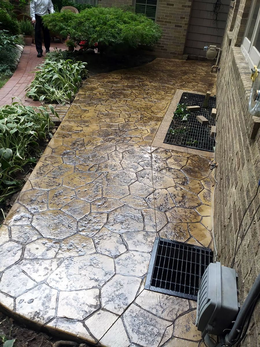 A concrete walkway leading to a house with a drain on the side of it.